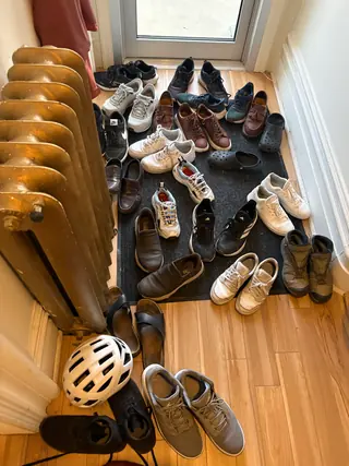 A pile of shoes and a bike helmet on the floor by an entrance door and a radiator.